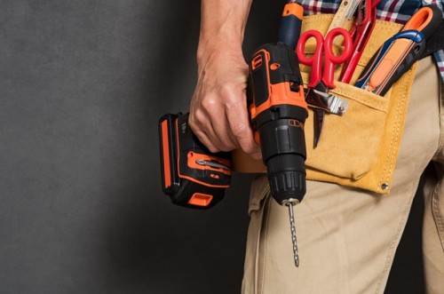GettyImages-901093256 - Close up of handyman holding a drill machine with tool belt around waist. Detail of artisan hand holding electric drill with tools isolated over grey background. Closeup hand of bricklayer holding carpentry accessories. (Close up of handyman holding a GettyImages-901093256