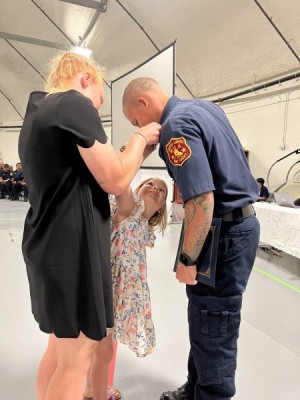 Lauren_Rowan_Donovan Dillon_DMC CCFD Pinning for EMT Paramedic Certification_051222 - During a May 12 ceremony, Lauren Dillon (left) and daughter Rowan pin husband Donovan Dillon after he completed the Del Mar College Emergency Medical Services Program’s Emergency Medical Technician-Paramedic certification pilot program. Dillon is one of 22 Corpus Christi Fire Department cadets to participate in the College’s innovative program that is the first in Texas and the nation and expedites training so that individuals can earn their EMT and Paramedic certification simultaneously. (Credit: DMC Digital Services) Lauren_Rowan_Donovan Dillon_DMC CCFD Pinning for EMT Paramedic Certification_051222