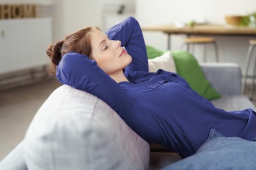 make renting out your home a breeze this summer - Attractive woman resting on a sofa at home lying back against the cushions with her hands clasped behind her head and eyes closed; Shutterstock ID 333515342; PO: .; Job: .; Client: .; Other: . make renting out your home a breeze this summer