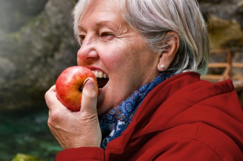 Seniors vitamins - Healthy looking senior woman with grey hair eating apple outside in the park ; Shutterstock ID 771172720 Seniors vitamins