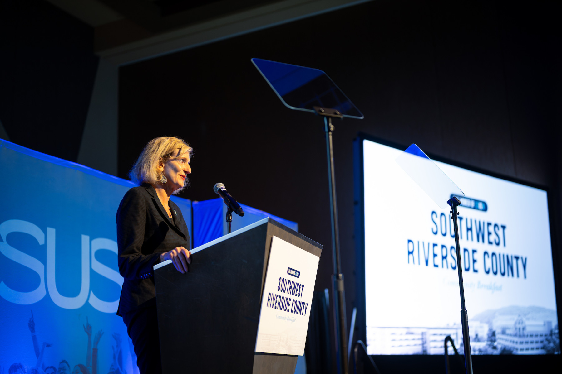 A woman speaking at a podium labeled "Southwest Riverside County" during a formal event