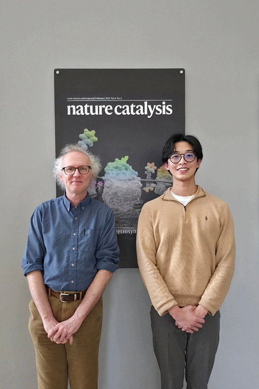 Dr Sam de Visser (L) and Henrik Wong (R) stand in front of a Nature Catalysis poster.