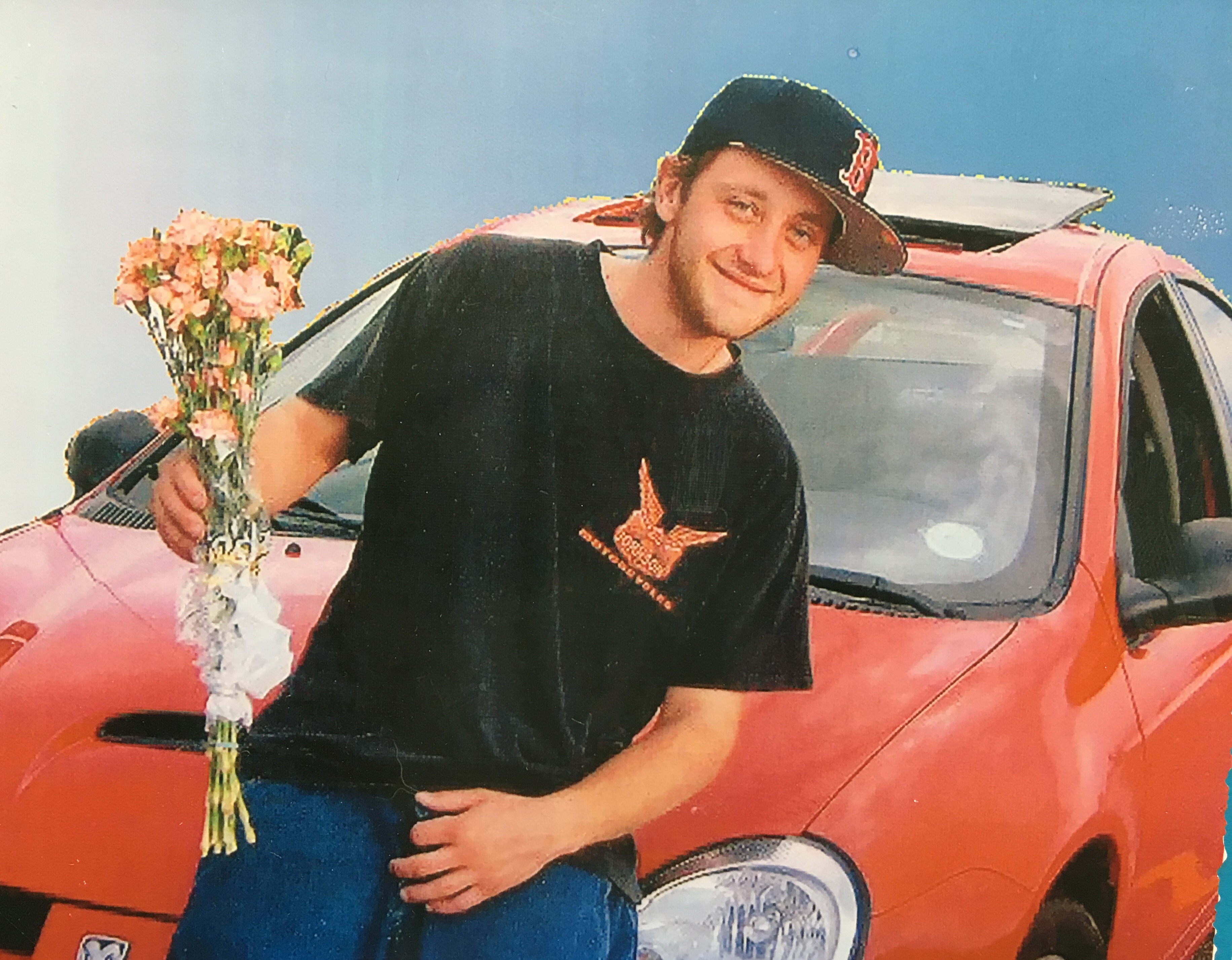 Zachary smiling, holding flowers, next to his Dodge Neon