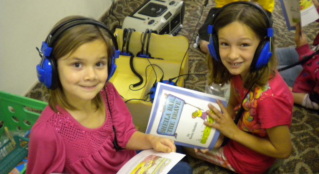 Two second grade girls listening to an audio book with headphones on.