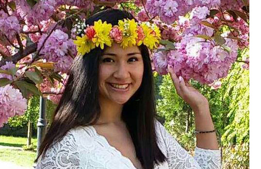 A photo of Selena Martinez smiling next to a flowering tree and with a band of flowers around her head.