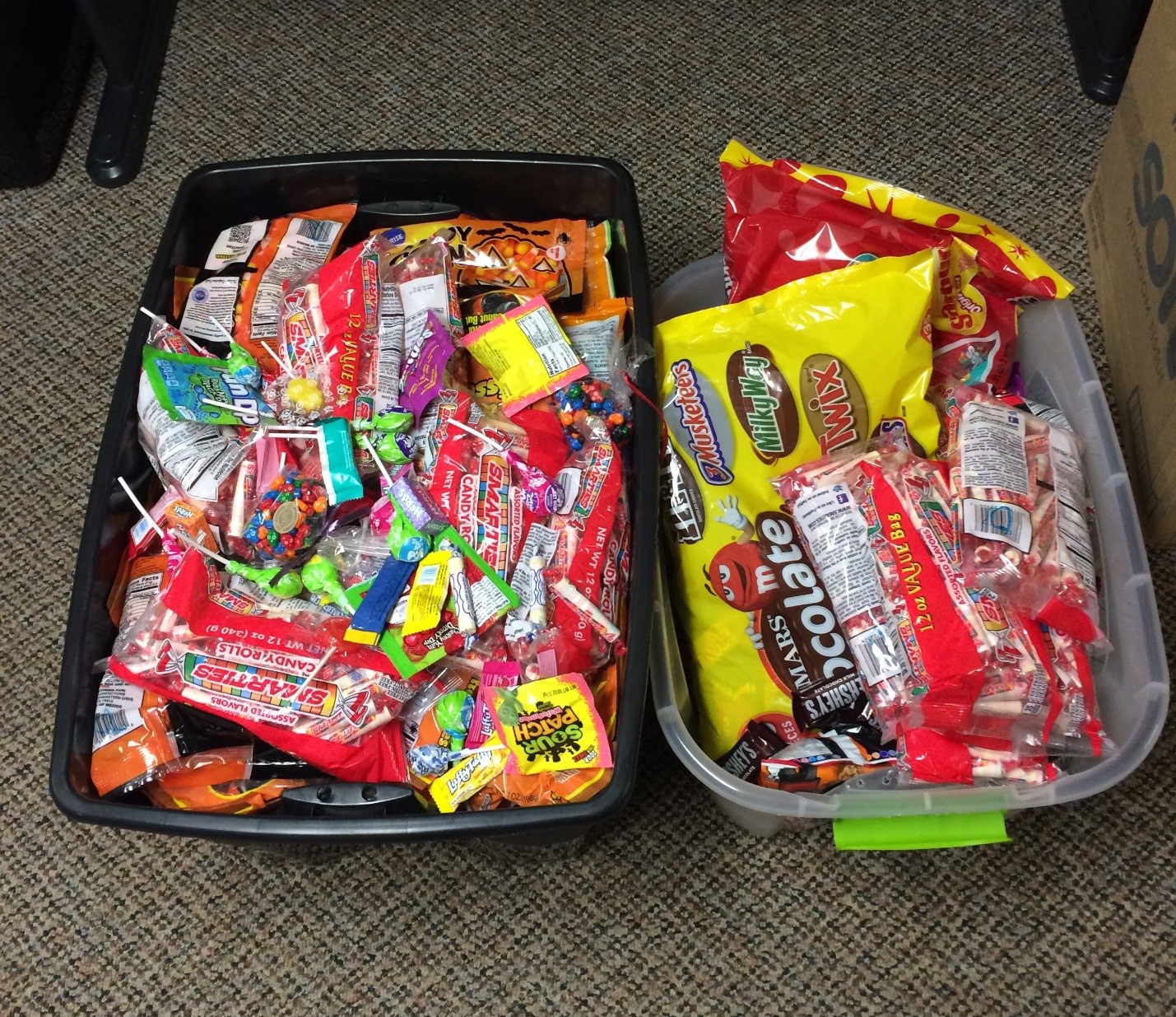 2 plastic bins of Halloween candy lying on the floor