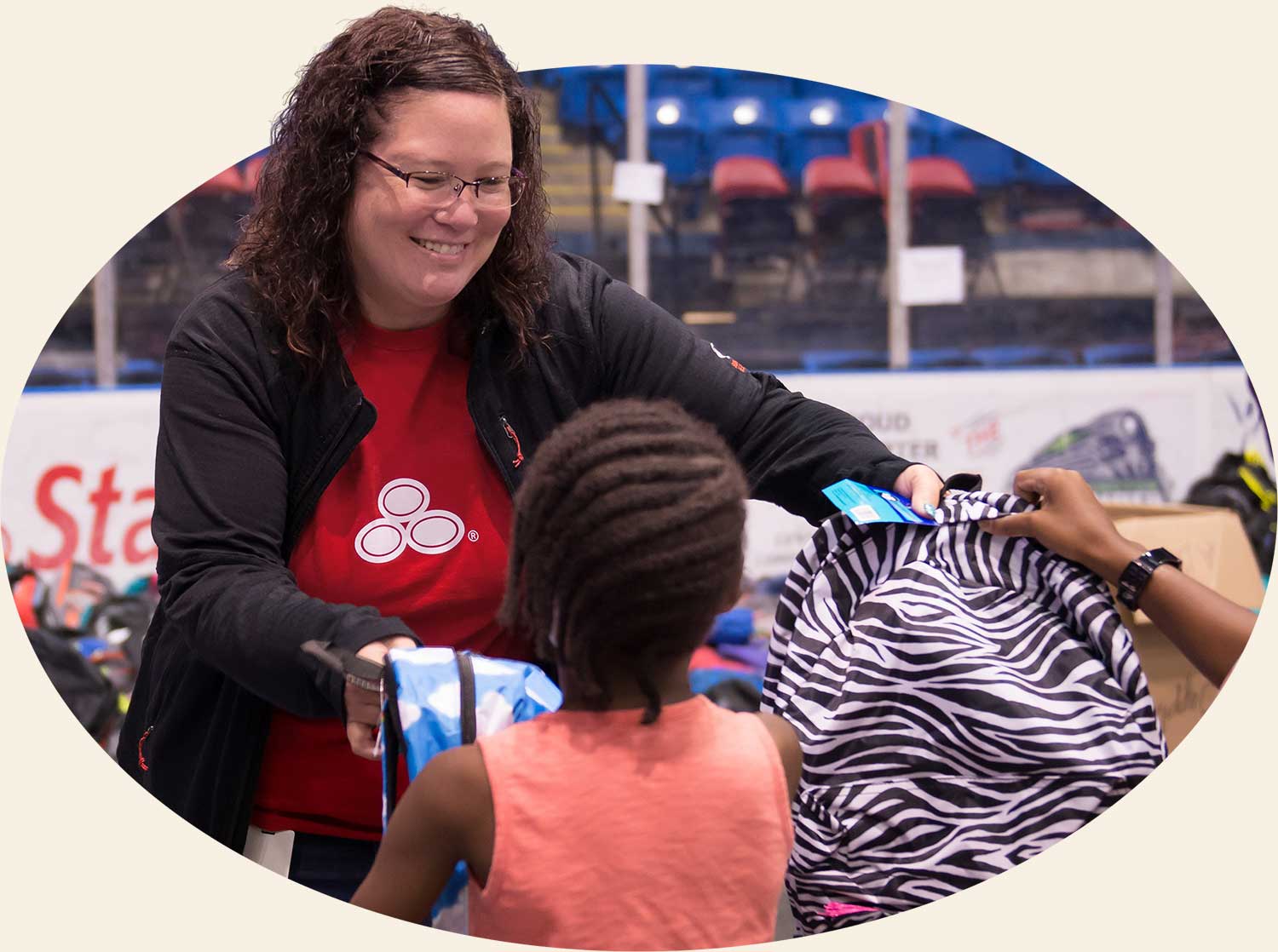 A photo of a woman passing out backpacks to kids