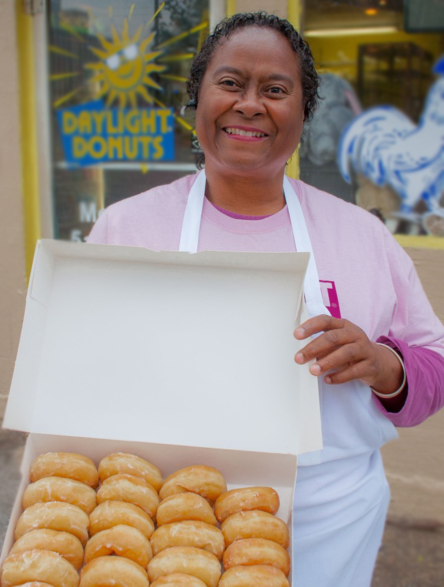 Debra Dickens Holmes holding a box of glazed donuts.