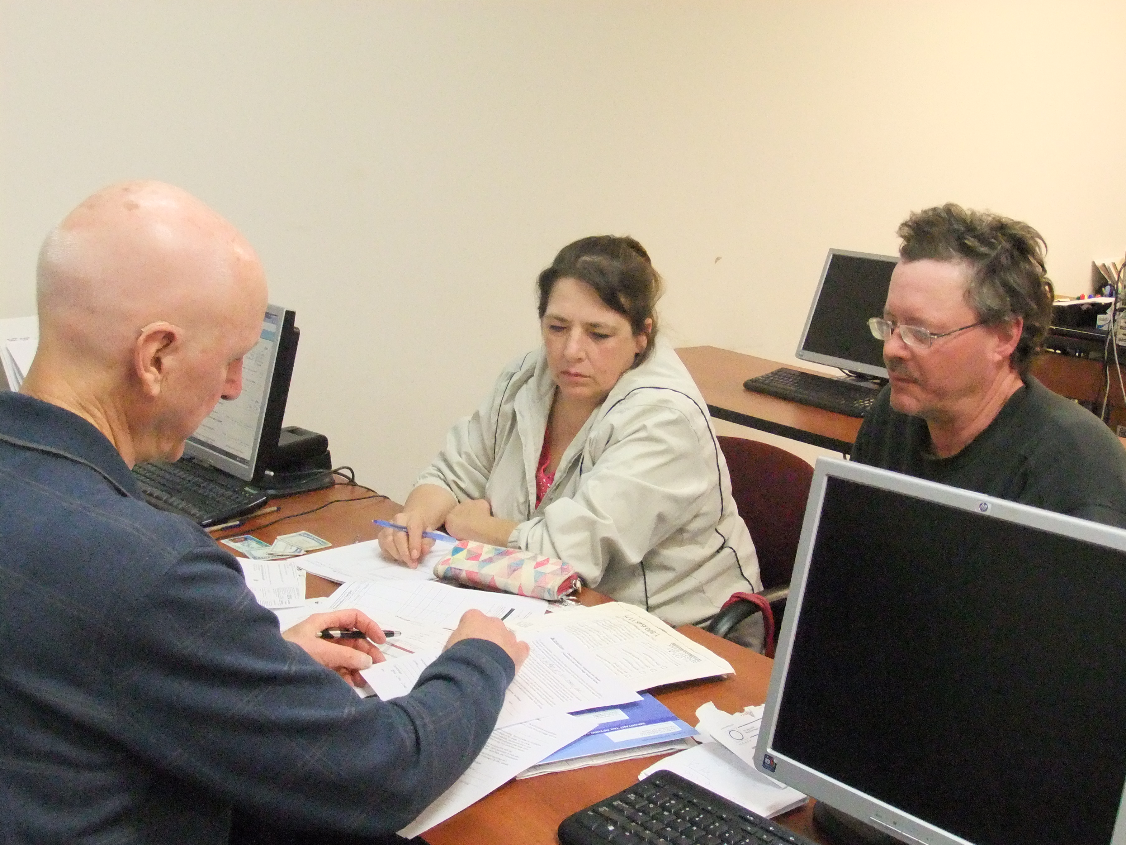 Man sitting across a table from a man and woman with papers in front him and they are all looking at the papers.