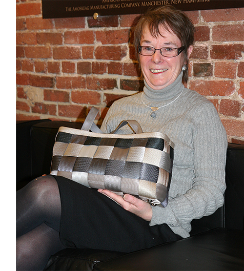 Women sitting next to a brick wall holding a purse made of seatbelts.
