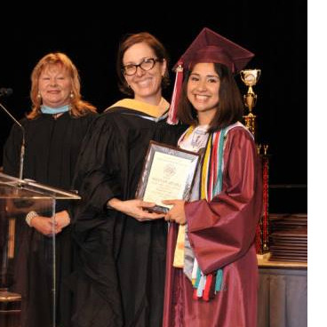 Selena Martinez in her cap and gown smiling as she is being presented her high school diploma by two school officials