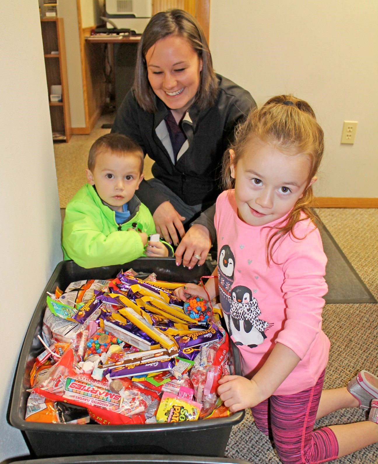 Smiling woman with two small children hovering over a plastic bin of Halloween candy