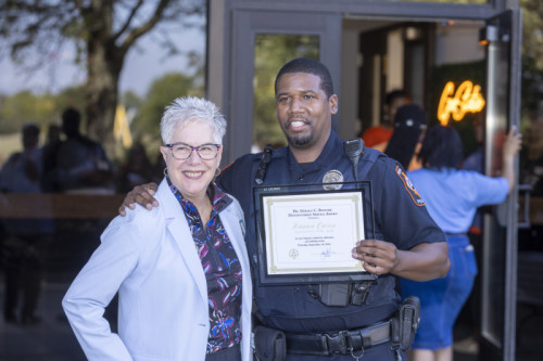 A smiling woman and man standing side by side while the man holds an award certificate