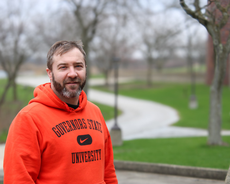 A man wearing an orange Governors State University hoodie standing outside