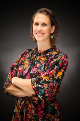 Professional headshot of a smiling woman wearing a pink orange and black floral dress