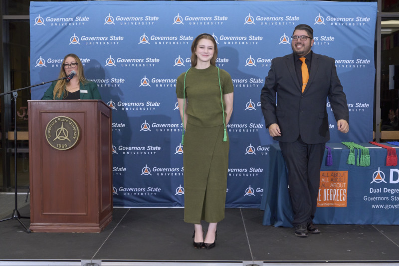 A student standing on a stage receiving a green cord for the dual degree program at Governors State University