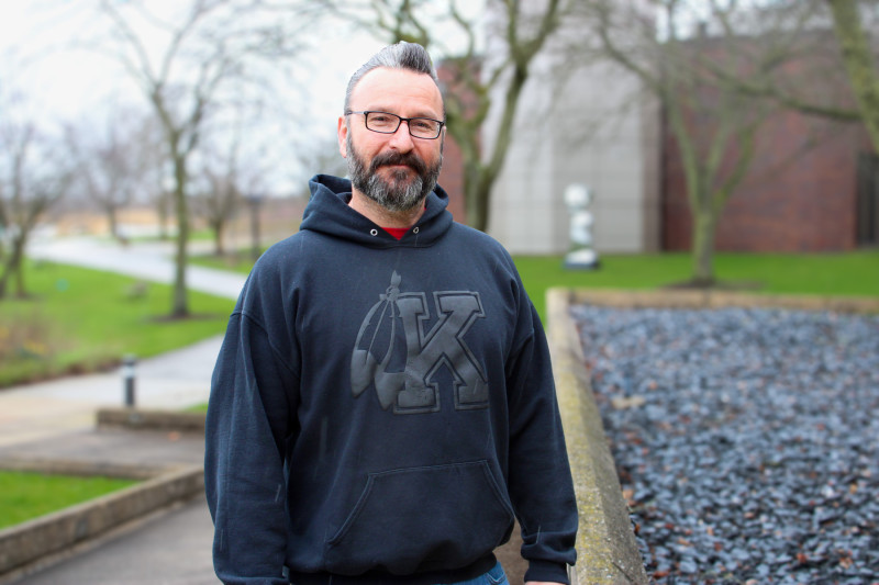 A man wearing glasses and a black hoodie standing on a sidewalk at Governors State University