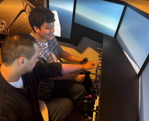 An aviation student showing his younger brother how to use a plane simulator