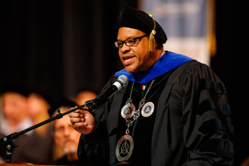A man in academic regalia speaking into a microphone