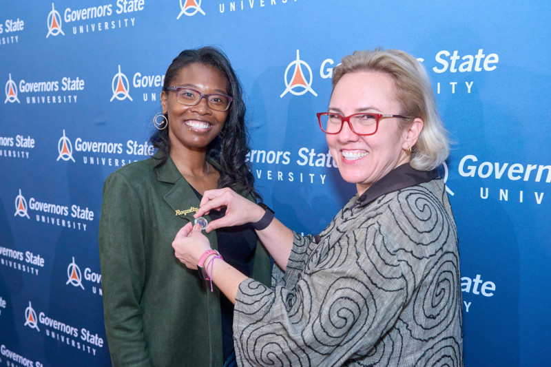 A Governors State University faculty member putting a pin on a student's jacket during a pinning ceremony