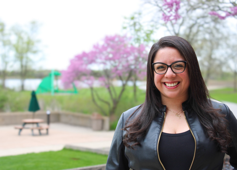 A smiling woman standing outside in front of trees with purple flowers