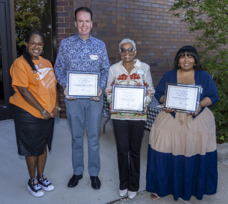 A smiling woman standing with a smiling man and two smiling women each holding award certificates