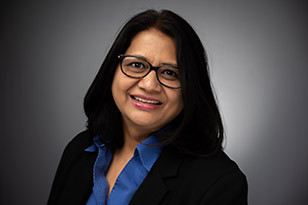 Headshot of a smiling woman wearing glasses with a blue shirt and black blazer