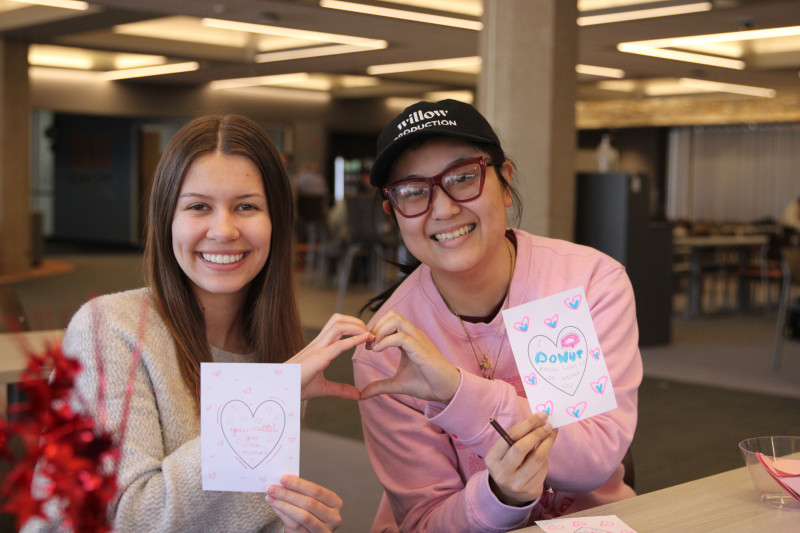 Two women making one heart together with their hands while holding handmade cards