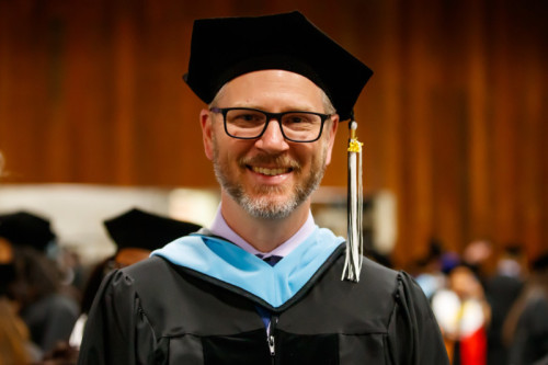 A smiling man wearing doctoral regalia