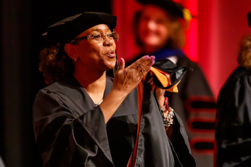 A woman in doctoral regalia blowing kisses to her friends and family