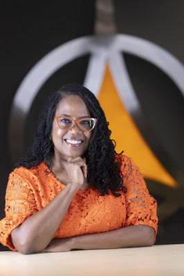 Portrait photo of a smiling woman wearing orange glasses and dress in front of the Governors State University Triad logo
