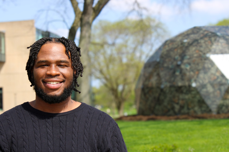 A smiling man standing in front of a dome shaped sculpture at Governors State University