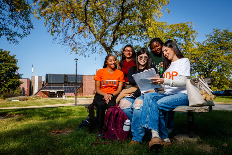 Five Governors State University students sitting on a bench outside on campus