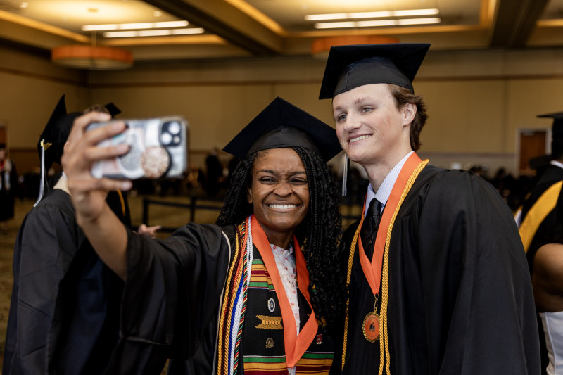 Two Governors State University graduates in regalia taking a selfie together