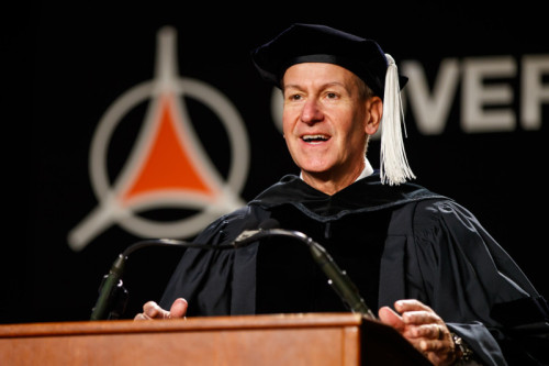 A man Phillip Kambic in academic regalia speaking at a podium for Governors State University 2025 Commencement