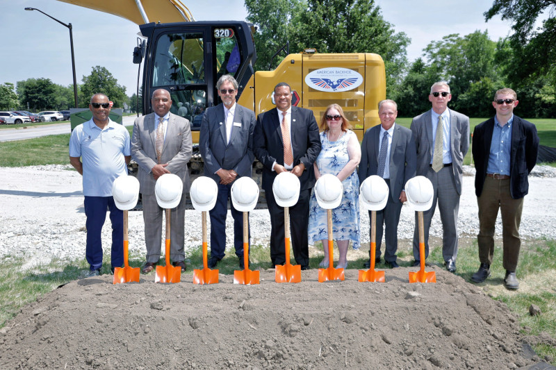 Seven men and one woman in business casual clothes standing by a pile of dirt that has shovels sticking up from it for a groundbreaking ceremony