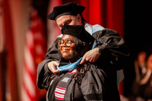 A woman in doctoral regalia smiling with her eyes closed as she receives her hood