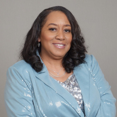 Headshot of a smiling woman wearing a light blue blazer and silver top