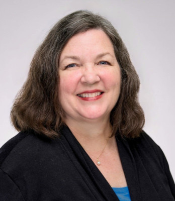 Professional headshot of a smiling woman wearing a black blazer and blue shirt
