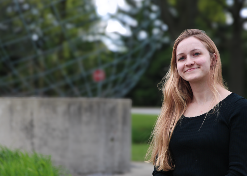 Portrait photo of a smiling woman standing in front of a sculpture on the Governors State University campus