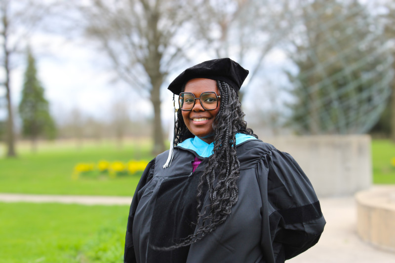 A smiling woman wearing a black graduation cap and gown