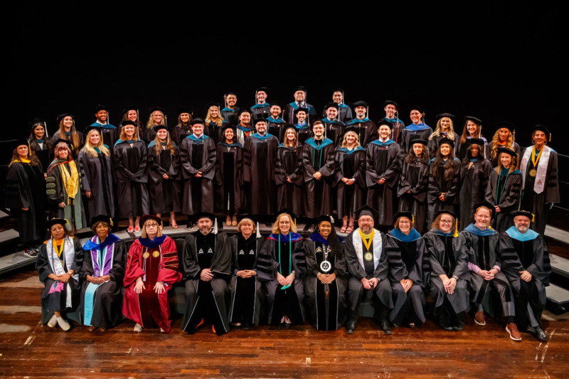 A group of people arranged in rows, some seated and some standing, wearing doctoral regalia