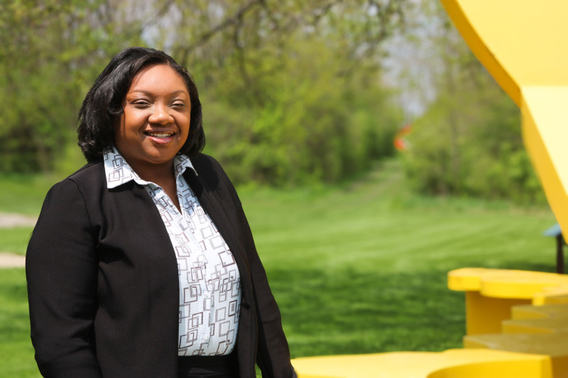 Portrait photo of a smiling woman wearing business casual clothes standing by a yellow sculpture