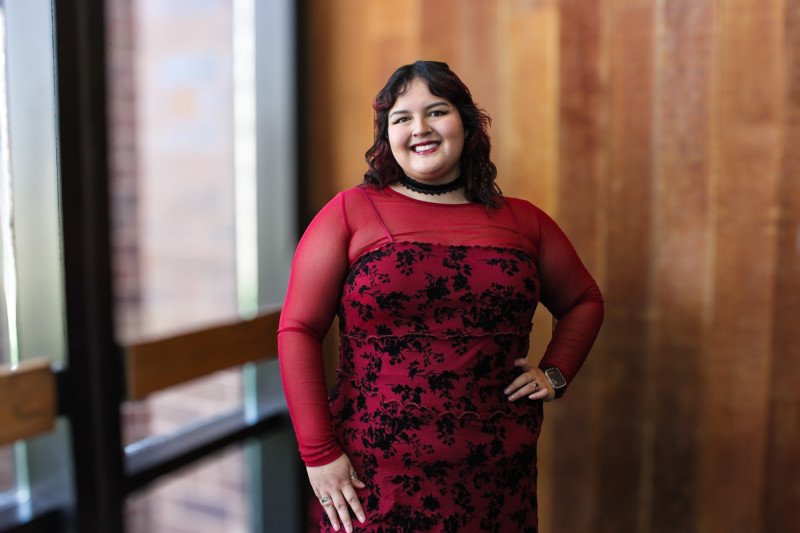 A smiling woman wearing a red dress standing in front of a wooden wall