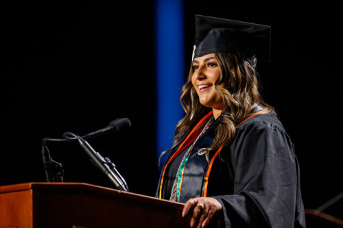 A woman Kaylie Dahms speaking at a podium for Governors State University 2025 Commencement