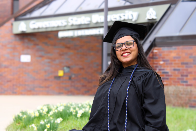 A smiling woman in cap and gown sitting in front of Governors State University