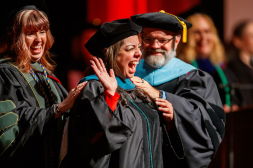 A woman in doctoral regalia smiling a waving as she receives her hood