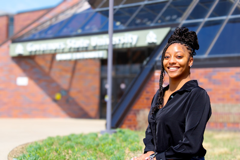 A smiling woman standing outside Governors State University's main entrance