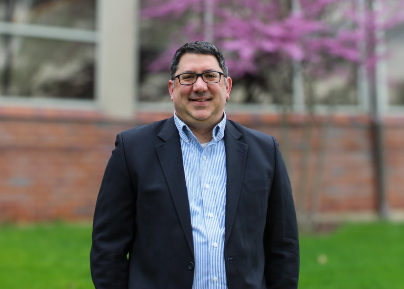 A smiling man in blue shirt and black blazer standing outside Governors State University