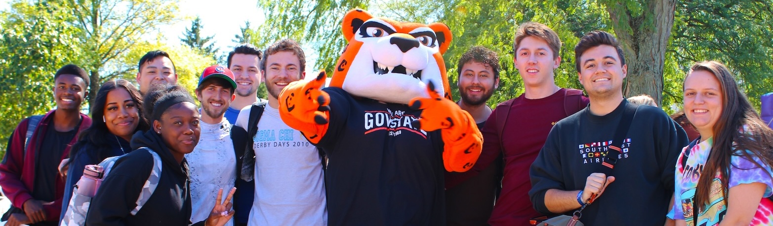 A group of diverse Governors State University students smiling for a photo with university mascot Jax the Jaguar